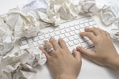 hands poised over keyboard surrounded by crumpled papers